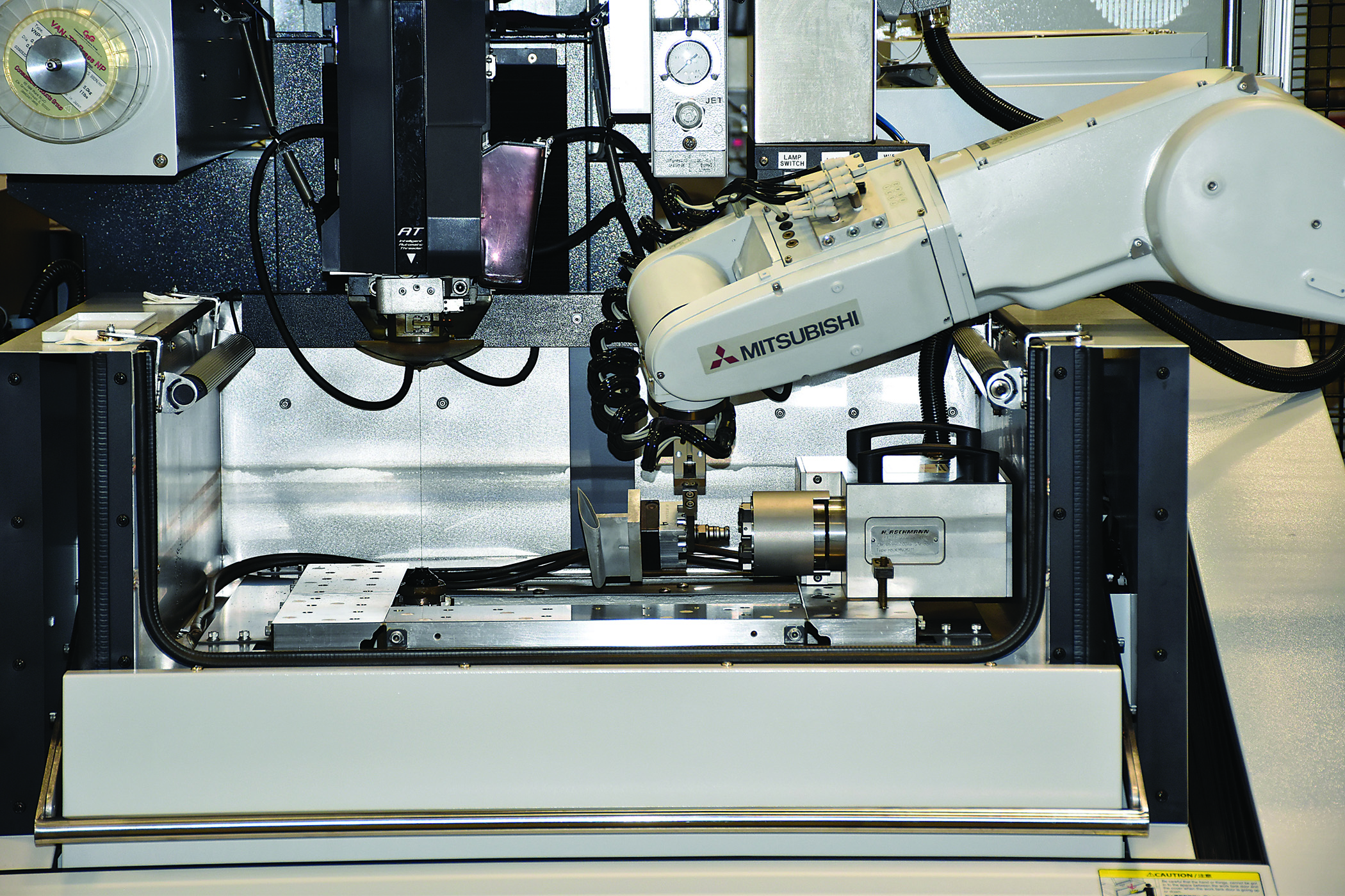 A Mitsubishi MELFA RV13F robot (above left) places a palletized production part into the tooling chuck of a rotary b-axis, which is mounted to the table of a Mitsubishi MV1200S wire EDM. 