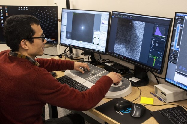 Xiaoqing He, a senior scientist at the Electron Microscopy Core Facility, works to adjust images from an electron microscope showing an experiment happening in real time.